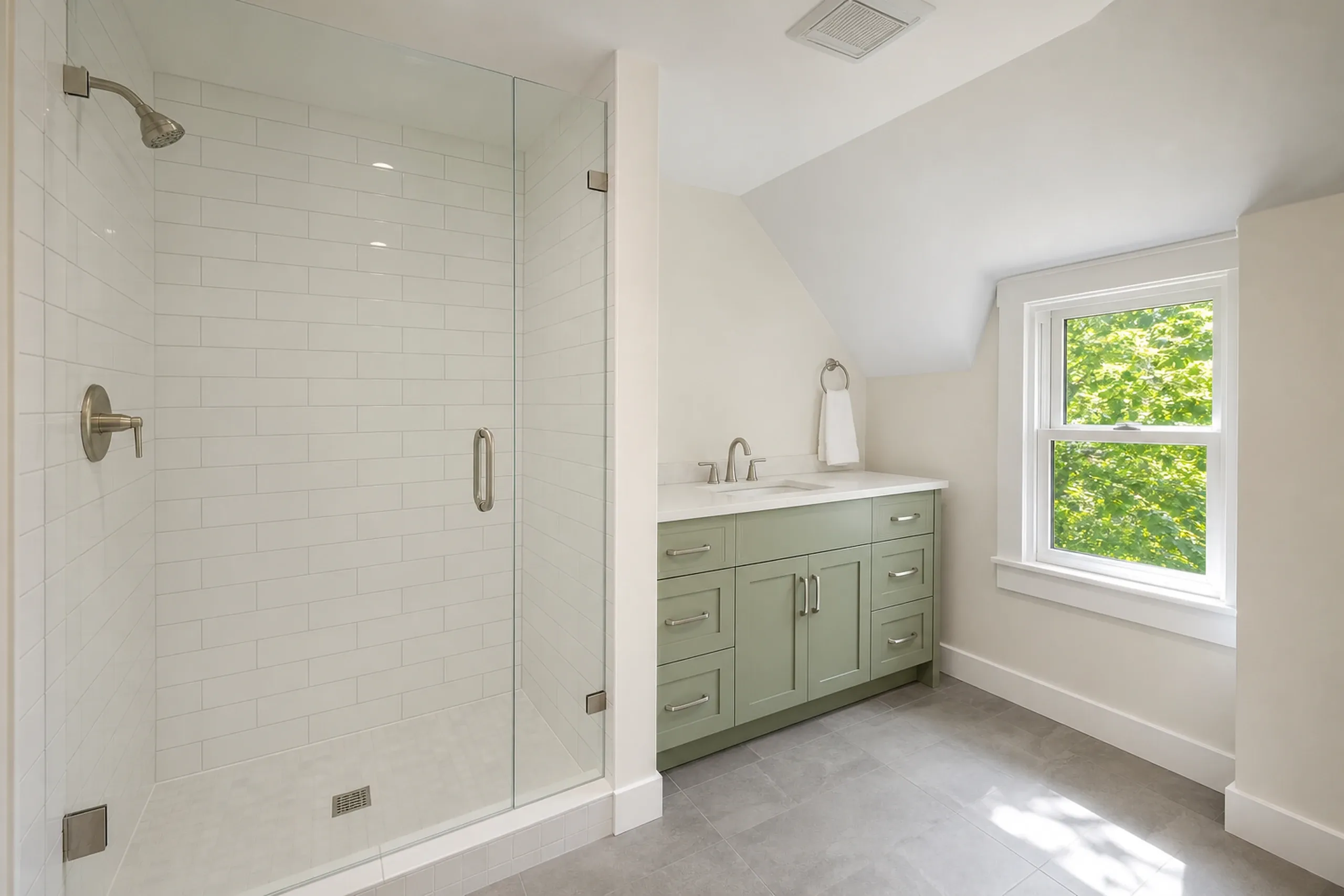 Master Bathroom Renovation in Clifton, ME: Interior view of a bathroom with a large walk-in shower with white subway tile, green vanity cabinet, white countertop, and a large window overlooking trees.