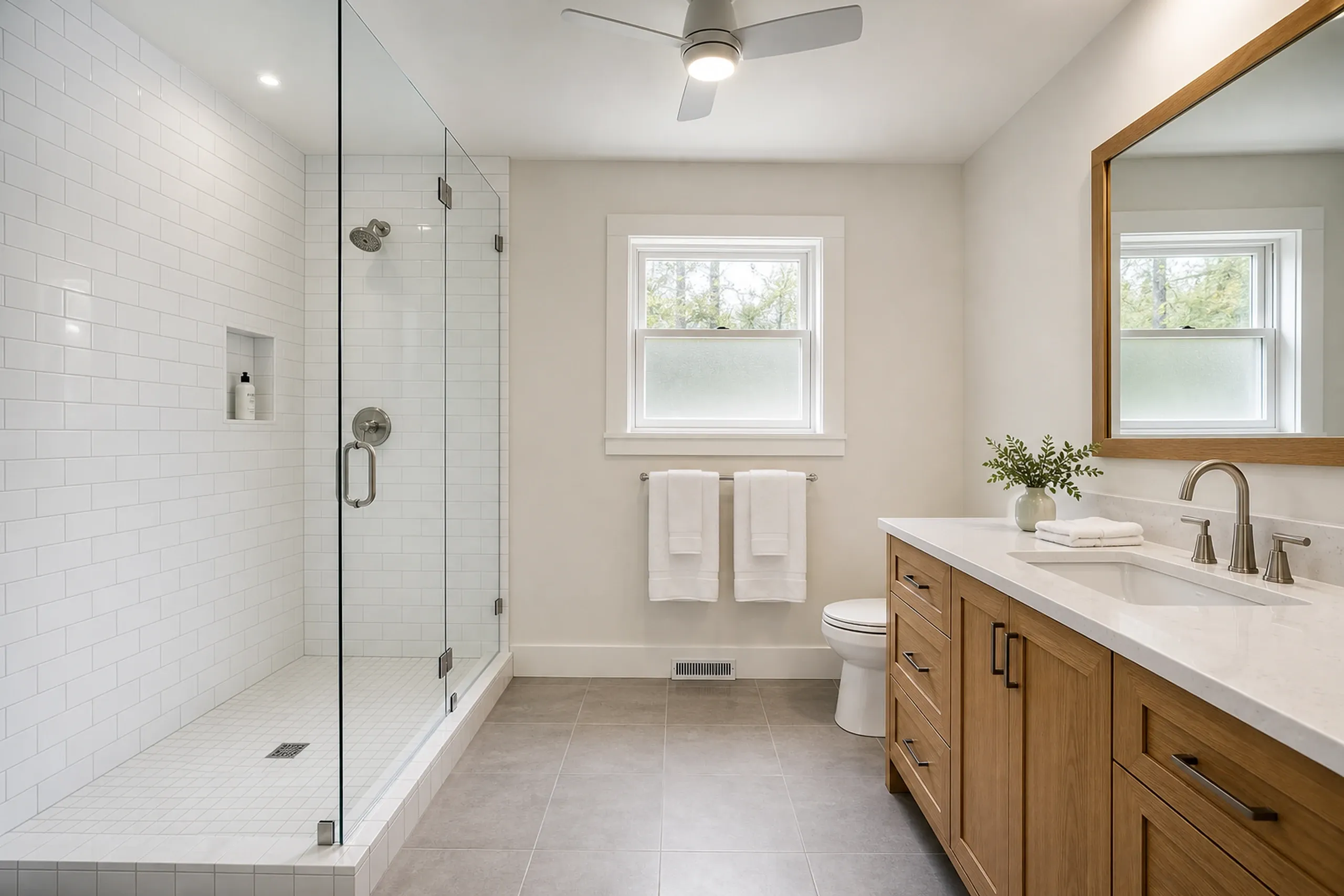 Primary Bathroom Remodel in Eddington, ME: Newly renovated bathroom with white subway tile shower, wood vanity, white countertop, and windows overlooking trees.
