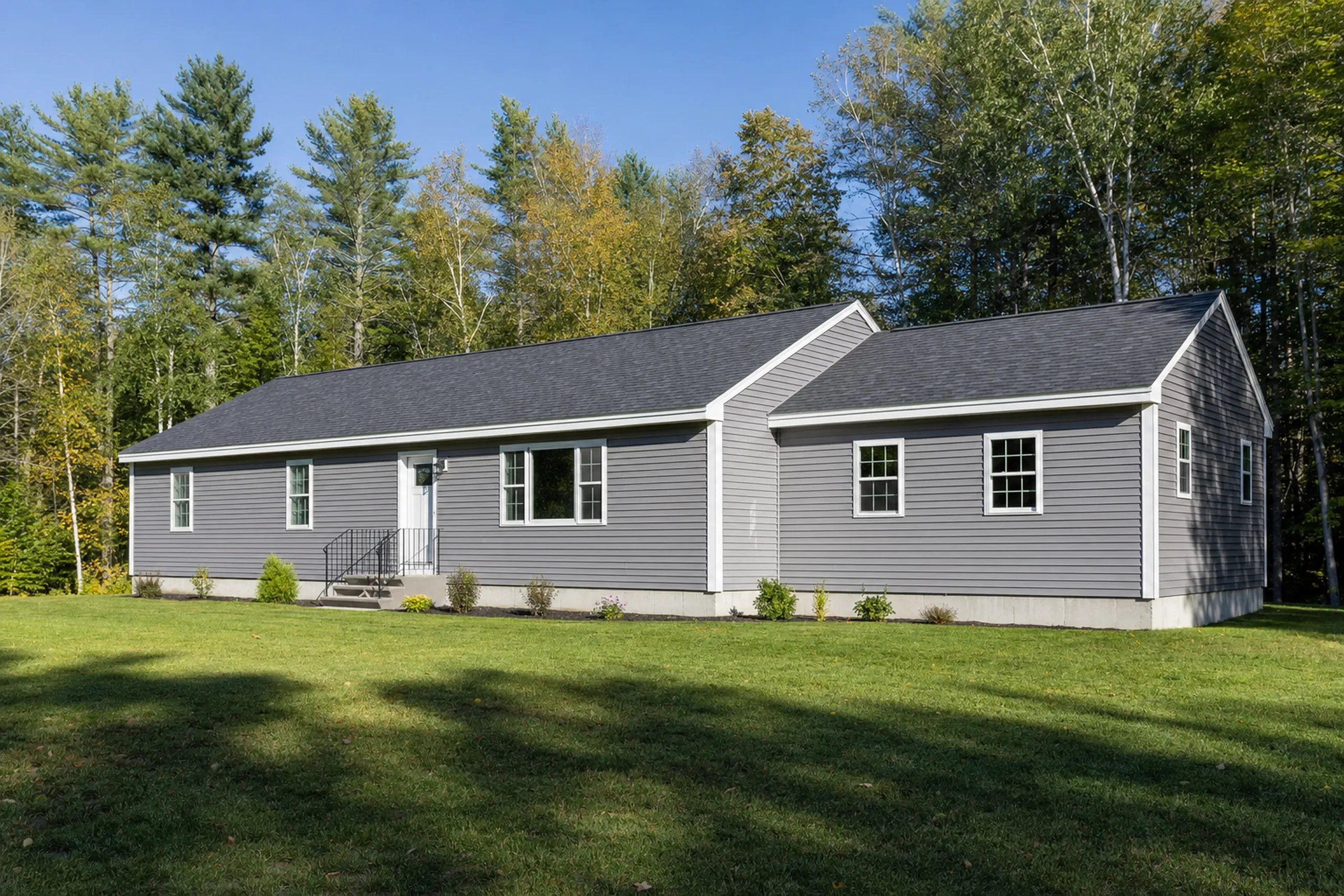 General contractor in Glenburn, ME: Single-story residential home with gray vinyl siding, white trim, and dark gray roof on a grassy lot surrounded by trees.