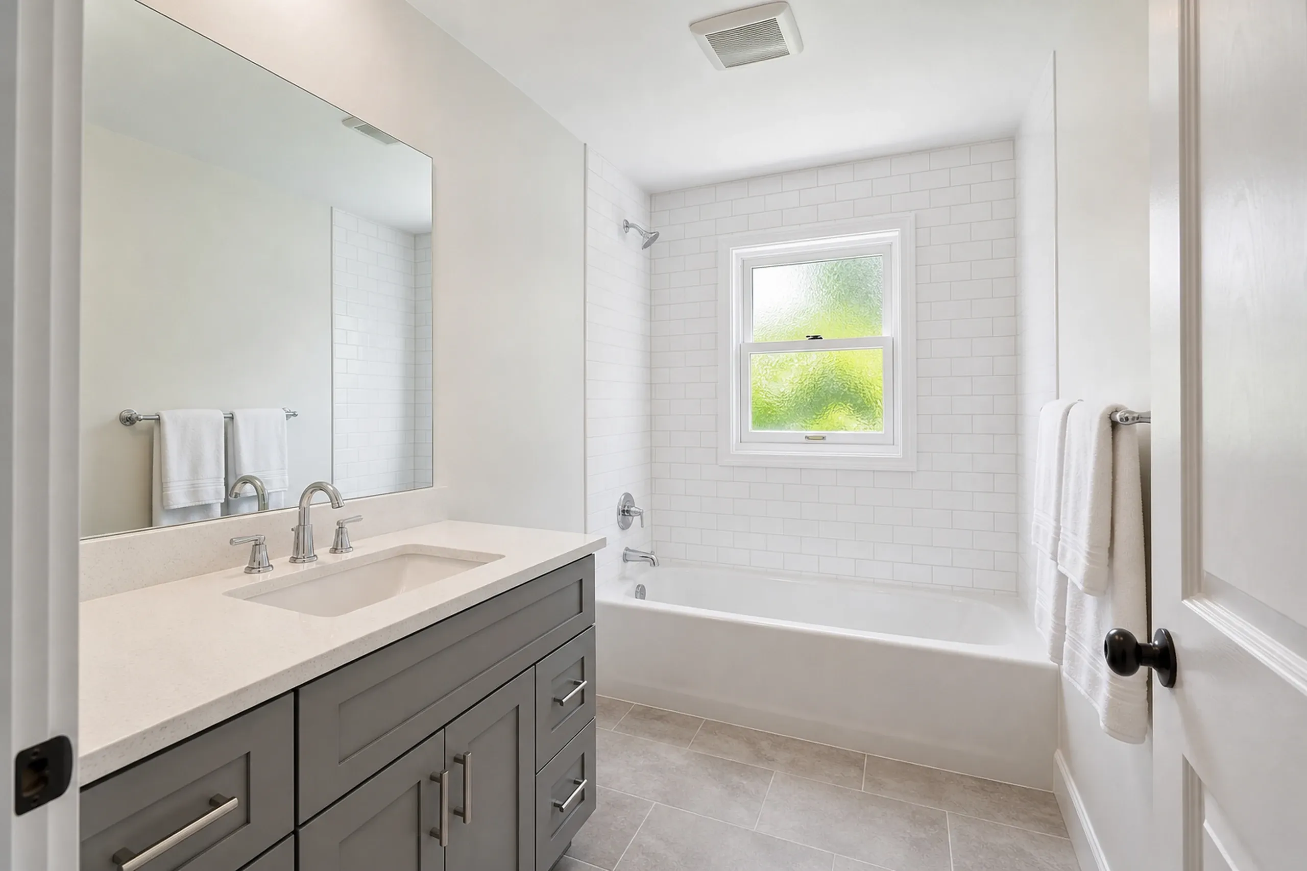 Bathroom renovation in Levant, ME: Interior view of a white subway tile bathroom with gray vanity, white countertop, and bathtub with window.