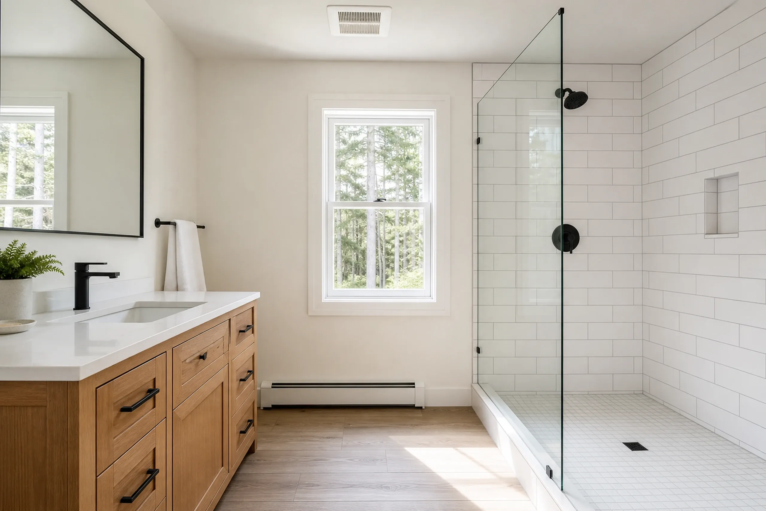 Modern bathroom in Newburgh, ME: Renovated bathroom with white subway tile walls, wooden vanity, black fixtures, glass shower enclosure, and window overlooking trees.